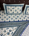 A blue and white patterned cotton bedspread set with matching pillowcases, styled on a bed with a dark brown tufted headboard.