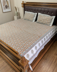 A bed dressed in a patterned cotton sheet and matching pillowcases, shown in a bedroom setting with a wooden bed frame and wood floor.