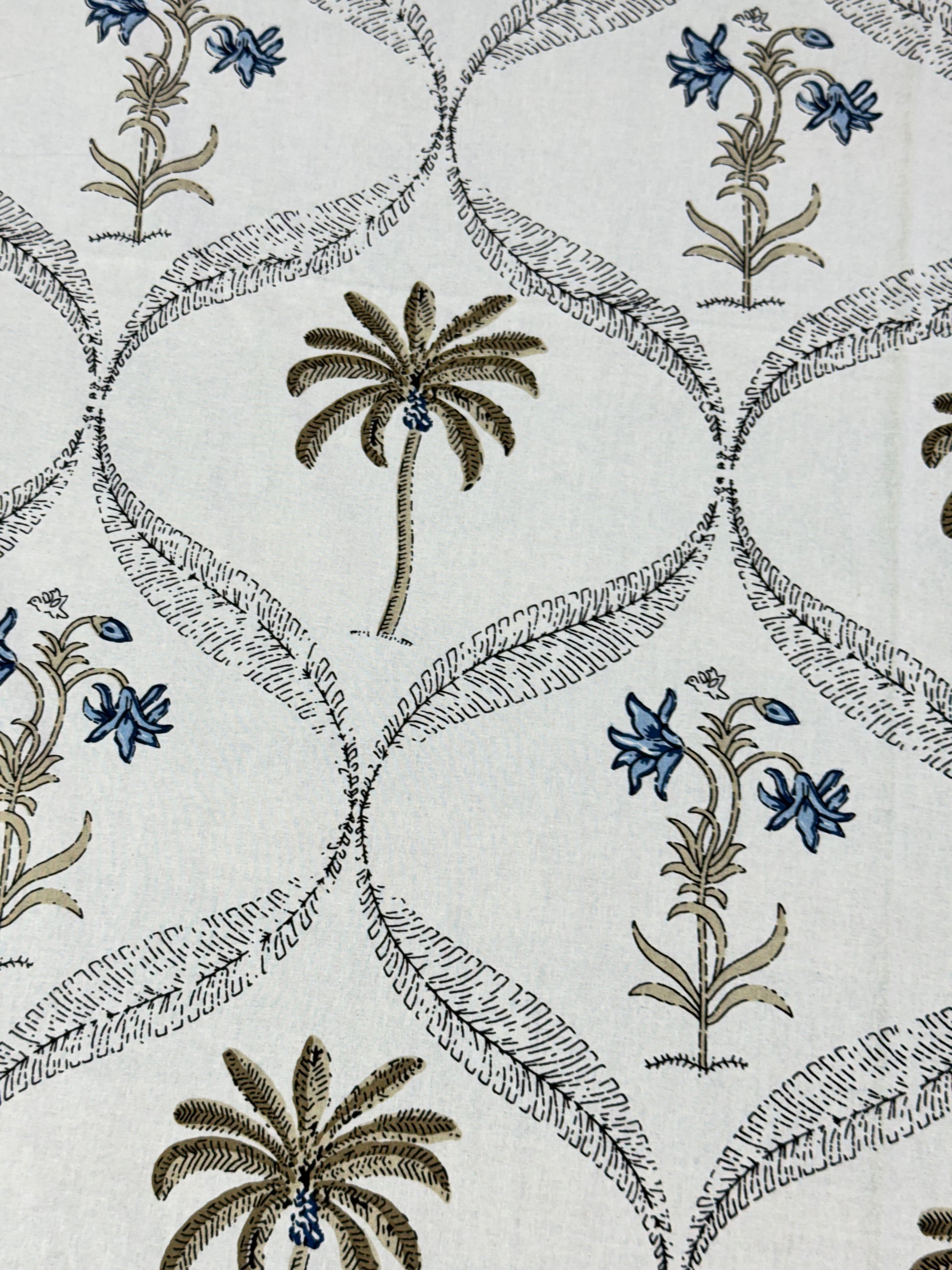 A close-up of a fabric or wallpaper pattern featuring palm trees and blue flowers arranged in an interlocking trellis design on a light cream background.